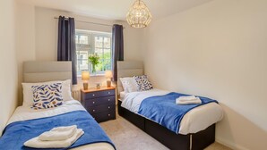 Une chambre avec deux lits, une commode, une fenêtre avec des rideaux et un luminaire suspendu.