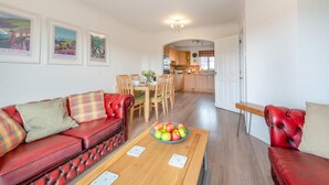 Una sala de estar con un sofá de cuero rojo, una mesa de centro de madera con un frutero y un comedor con sillas y mesa de madera.