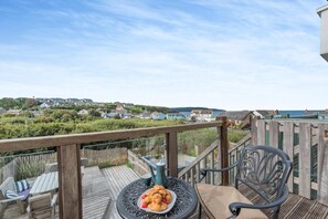En balkon med udsigt over en kystby, et bord med mad og udendørs siddepladser.