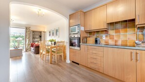 Una cocina moderna con armarios de madera, un comedor con mesa y sillas, y vistas al exterior a través de un ventanal amplio.
