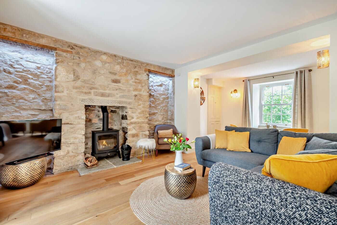A cozy living room with a stone fireplace, a sofa with yellow cushions, and a television on a wooden stand.