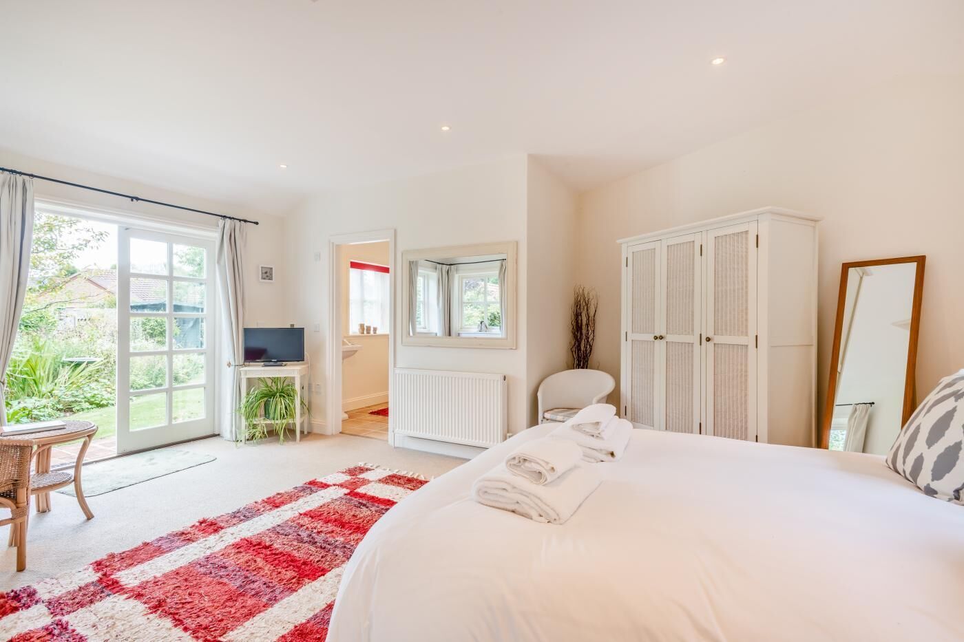 Une chambre avec un grand lit, une télévision, un fauteuil et une vue sur le jardin, accessible par une porte coulissante.