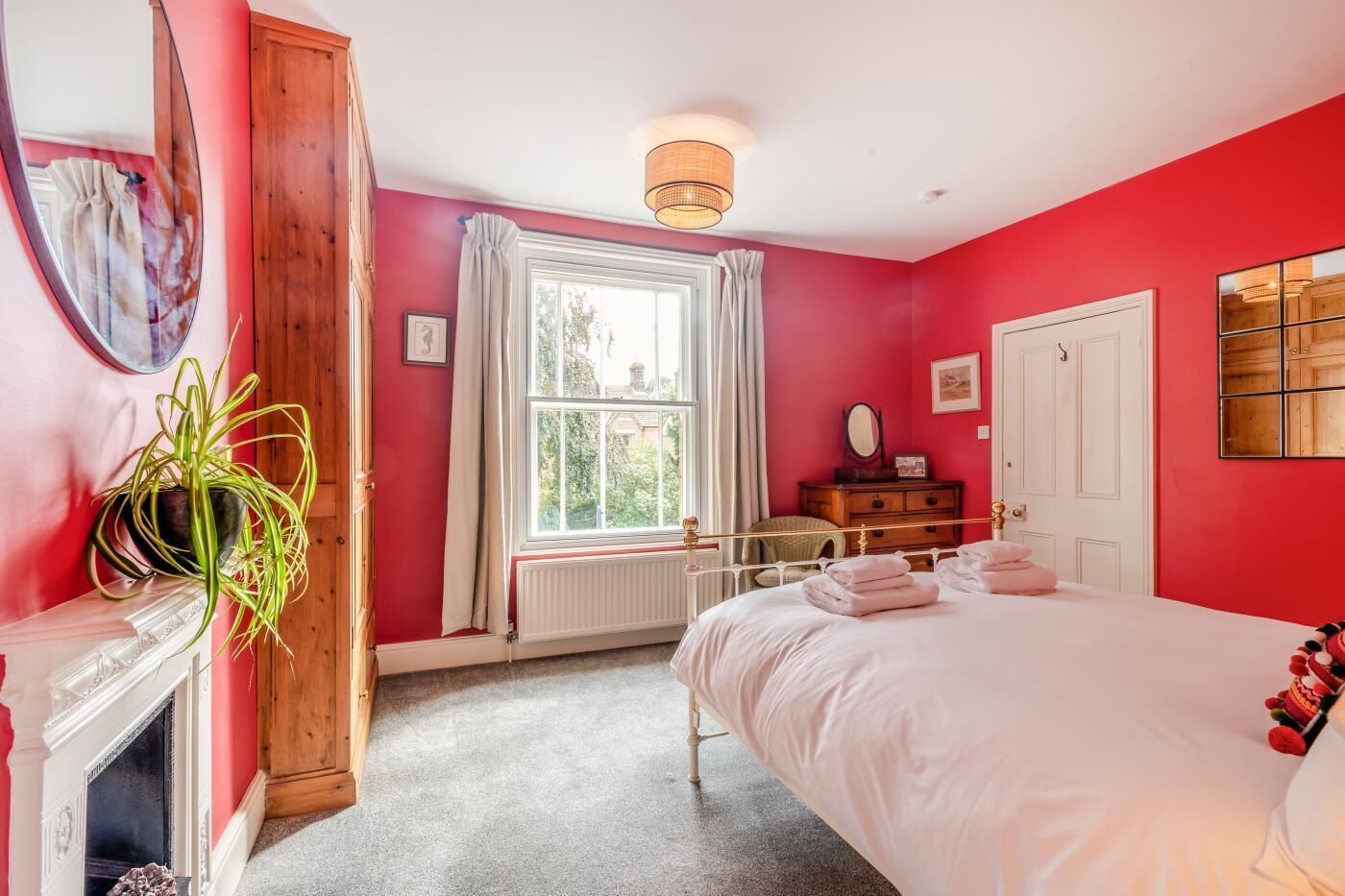 A bedroom with a bed, a dresser, a mirror, a window with curtains, a radiator, and a potted plant.