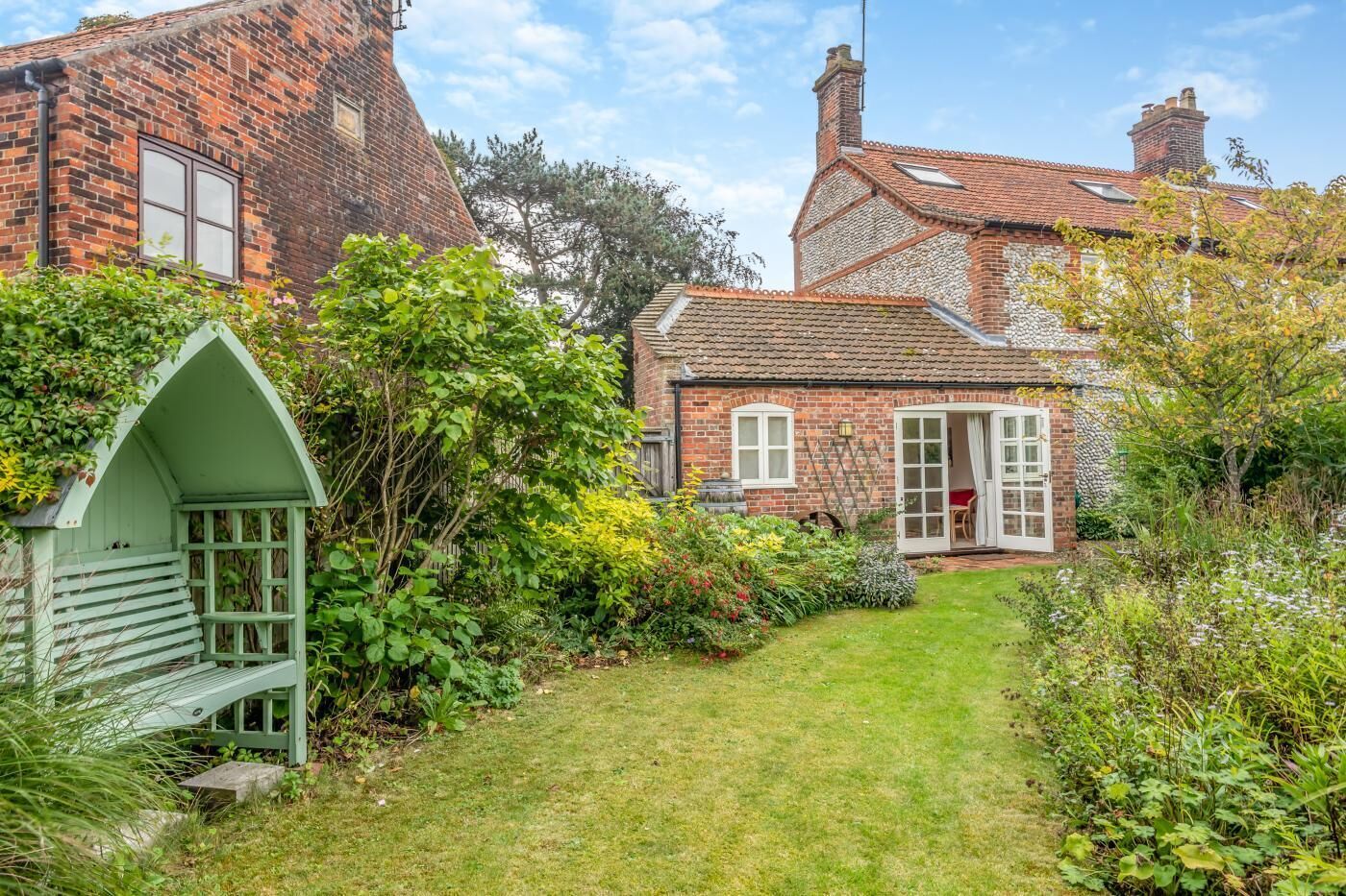 A traditional brick house with a well-maintained garden, a small wooden structure, and a clear pathway leading to the entrance.