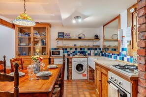 A compact kitchen with a wooden table, a washing machine, a microwave, and a stove. - 2 Bed in St Ives (oc-wrenc) (St Ives)
