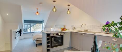 A modern kitchen with a built-in oven, a dining area with a table and chairs, and a small seating area with a bed.