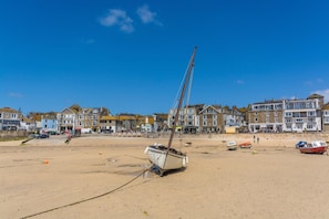 A beach with a sailboat, buildings, and a clear sky.