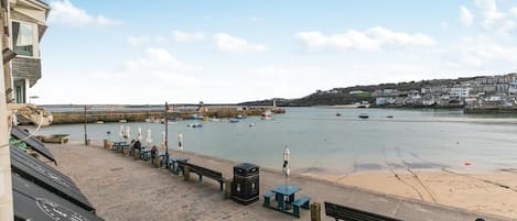 A waterfront promenade with benches, a sandy beach, and boats in the water.