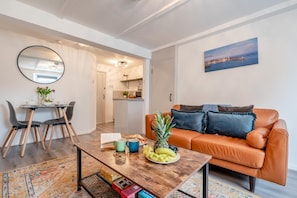 Una sala de estar moderna con una mesa de centro de madera, un sofá con cojines, un comedor con sillas y una cocina al fondo.