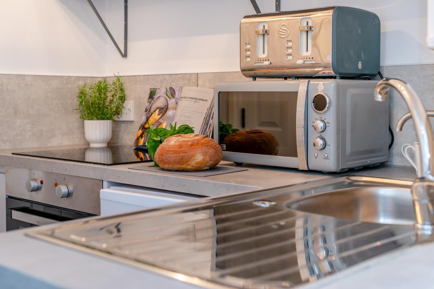 A kitchen with a stainless steel sink, a toaster, a microwave, and a loaf of bread on the counter.