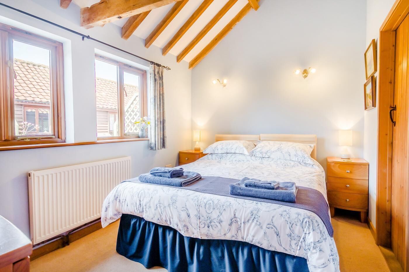A bedroom with a bed, two bedside tables, a window, and a radiator.