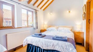 A bedroom with a bed, two bedside tables, a window, and a radiator.