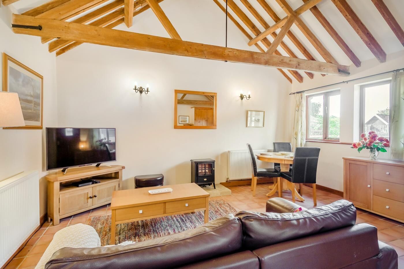 A cozy living room with a wooden ceiling, a flat-screen TV, a dining area with a table and chairs, and a leather sofa.