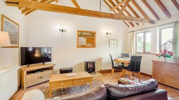 A cozy living room with a wooden ceiling, a flat-screen TV, a dining area with a table and chairs, and a leather sofa.