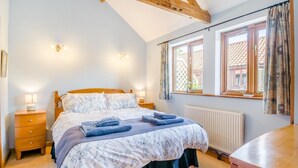 Una camera da letto con un letto, comodini, una finestra con tende e un trave in legno al soffitto.