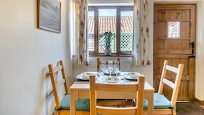 A dining area with a table set for four, wooden chairs with cushions, a window with floral curtains, and a view of a tiled roof outside. - 2 Bed in Wissett (oc-hfleet) (Wissett)