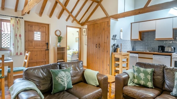 A cozy living room with a brown leather sofa, wooden beams on the ceiling, and a kitchen with white cabinets and a tiled backsplash. - 2 Bed in Wissett (oc-hfleet) (Wissett)