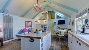 Una cocina con una isla de madera, una zona de comedor con sillas, un televisor montado en la pared y un techo con vigas a la vista.