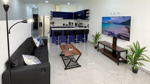 Una sala de estar moderna con un sofá negro, una mesa de centro de madera y un televisor en la pared.