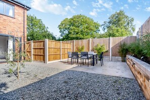 Ein Garten mit Terrasse, Holzzaun und Kiesfläche.