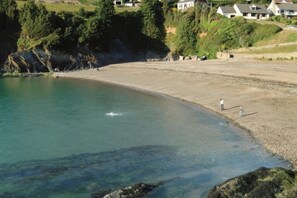 A coastal beach with clear water, a rocky shoreline, and houses in the background. - 1 Bed in Parracombe (oc-l28026) (Trentishoe)