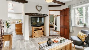 Sala de estar com televisão, painel para aparelhos eletrônicos de madeira e mesa de centro com um livro e caneca.