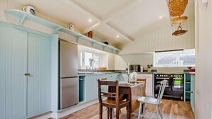 A modern kitchen with light blue cabinetry, a stainless steel refrigerator, a dining area with a wooden table and chairs, and a window providing natural light. - 2 Bed in Yoxford (oc-b27975) (Middleton Moor)