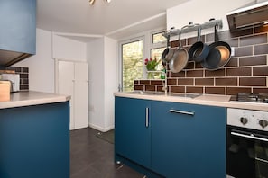 A modern kitchen with blue cabinets, a gas stove, and hanging pots. - 3 Bed in Little Haven (oc-h27960) (Little Haven)