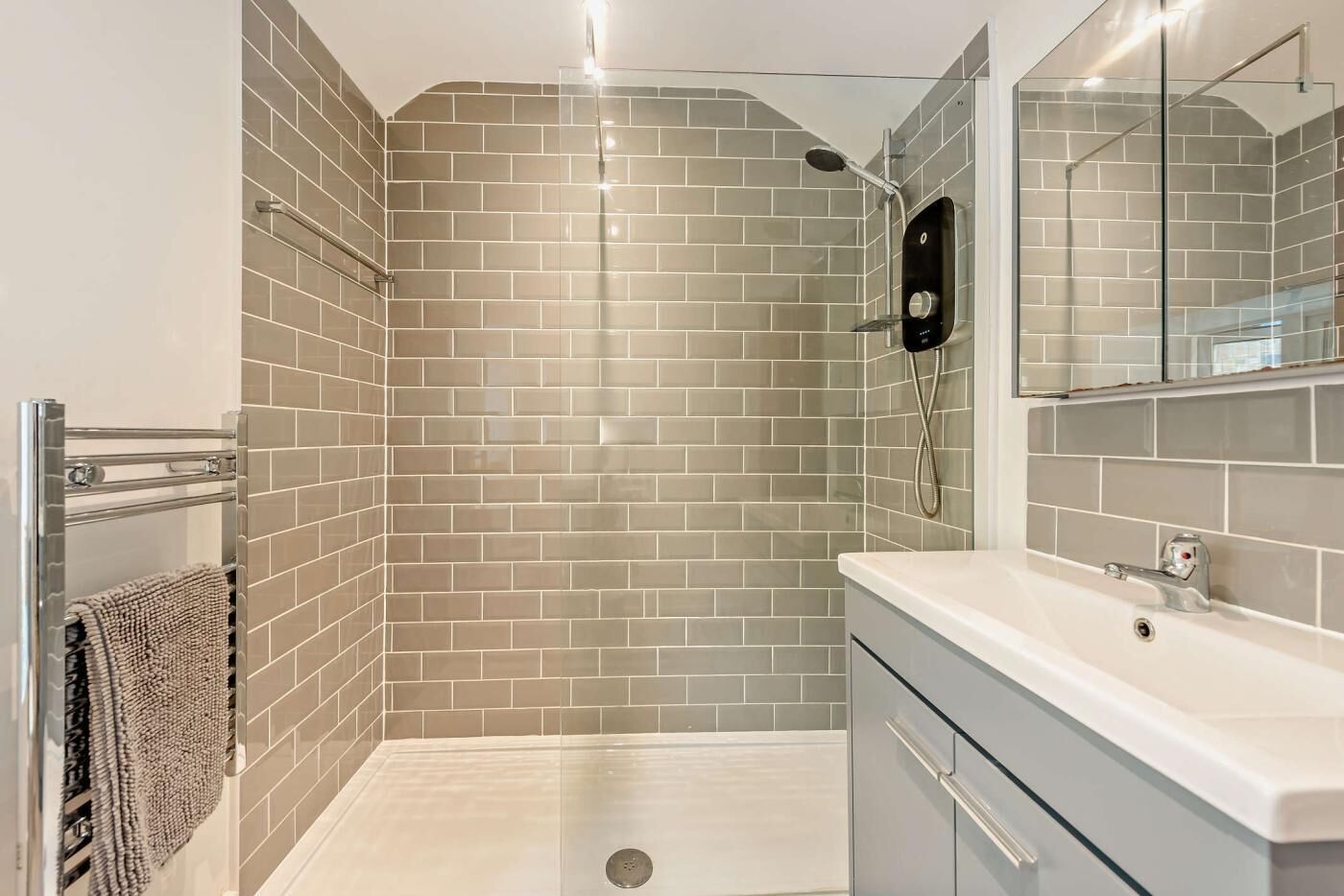 A modern bathroom with a shower, a glass-enclosed corner, a towel rack, and a sink with a mirror.