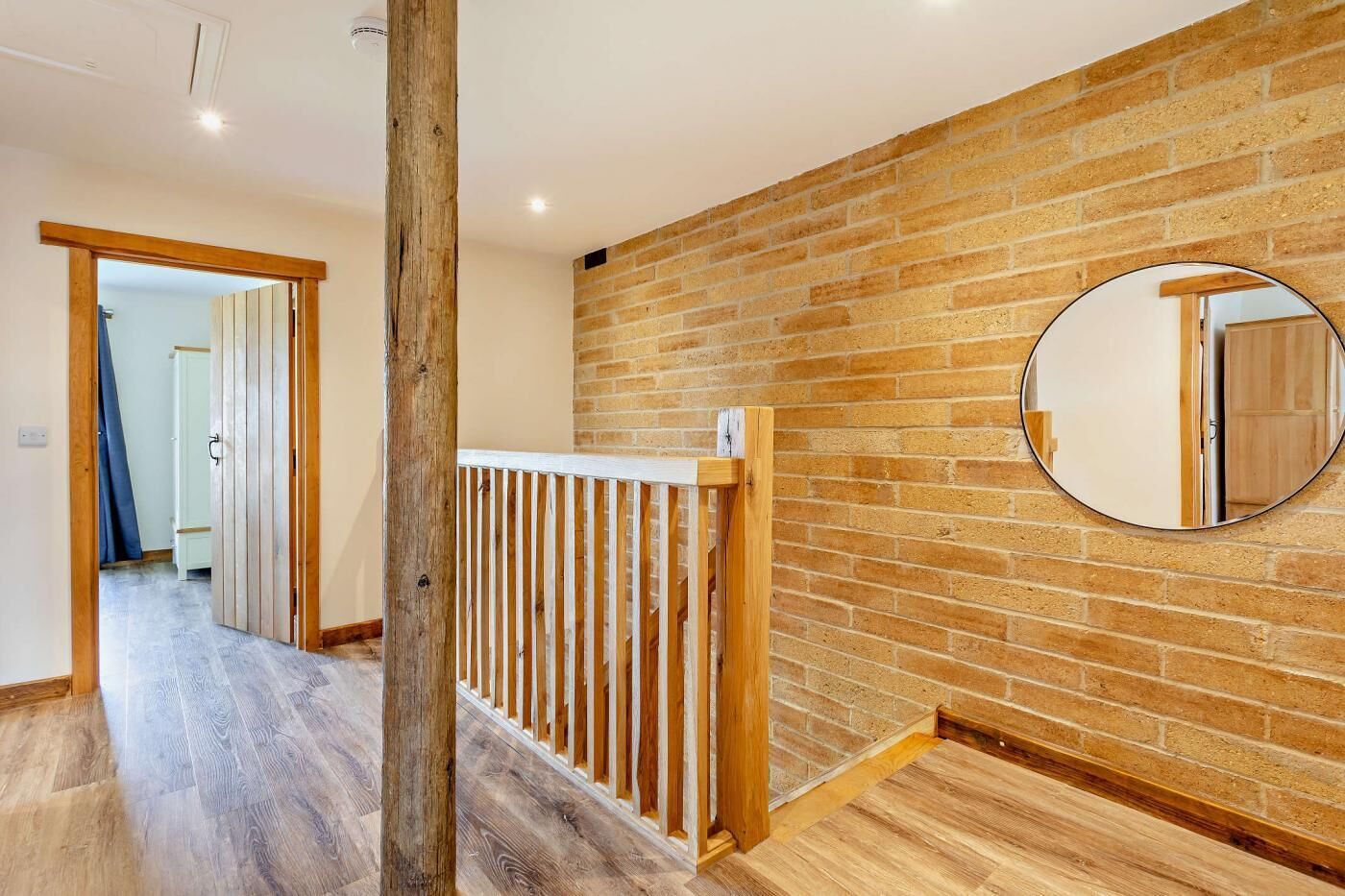 A hallway with a wooden floor, a brick wall, and a wooden railing.