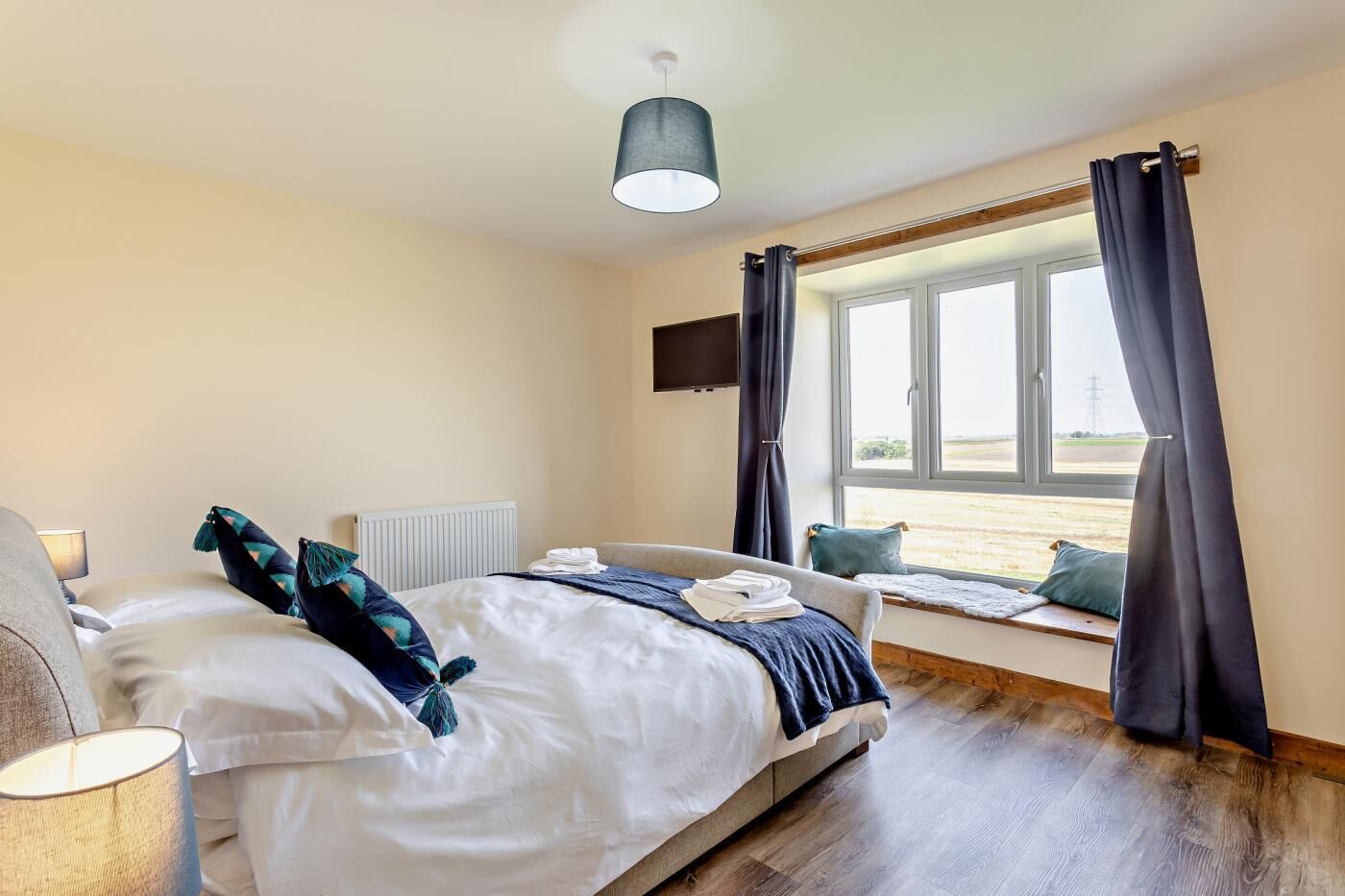 Un dormitorio con cama, ventana con cortinas, radiador y televisor montado.