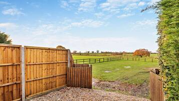 A wooden gate leading to a fenced field with a gravel path.