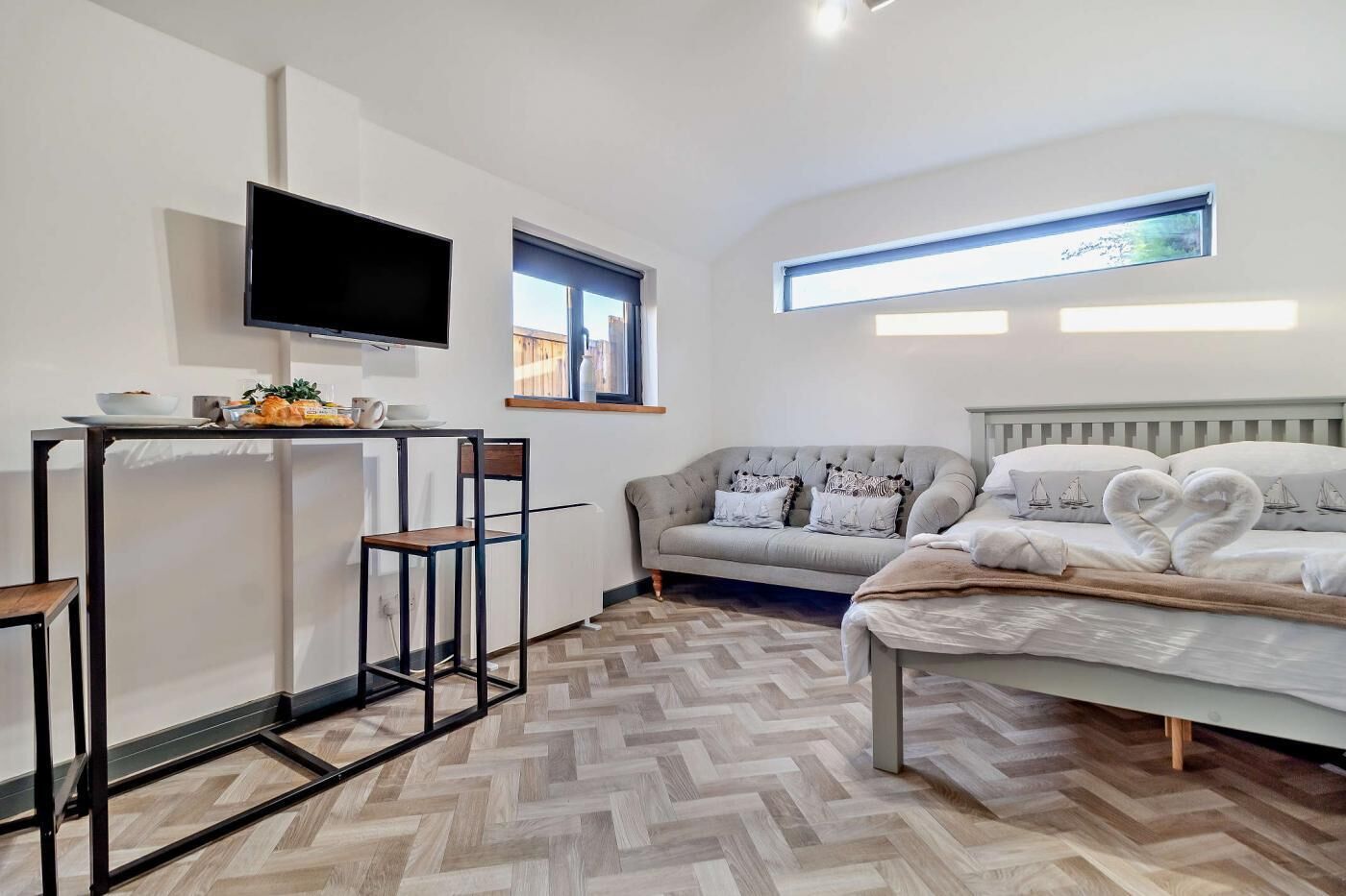 A modern bedroom with a bed, a sofa, a TV, and a small table with breakfast items.