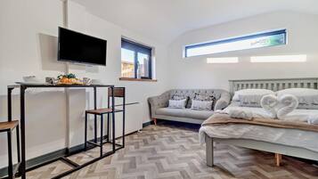 A modern bedroom with a bed, a sofa, a TV, and a small table with breakfast items.