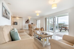 A modern living room with a sofa, a coffee table, and a dining area with a table and chairs. There is a kitchen in the background with cabinets and a refrigerator. - 2 Bed in Bournemouth (oc-b27914) (Bournemouth)