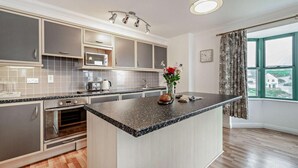 A modern kitchen with a central island, built-in appliances, and a view of the outside through a large window. - 2 Bed in Broad Haven (oc-s28021) (Broad Haven)