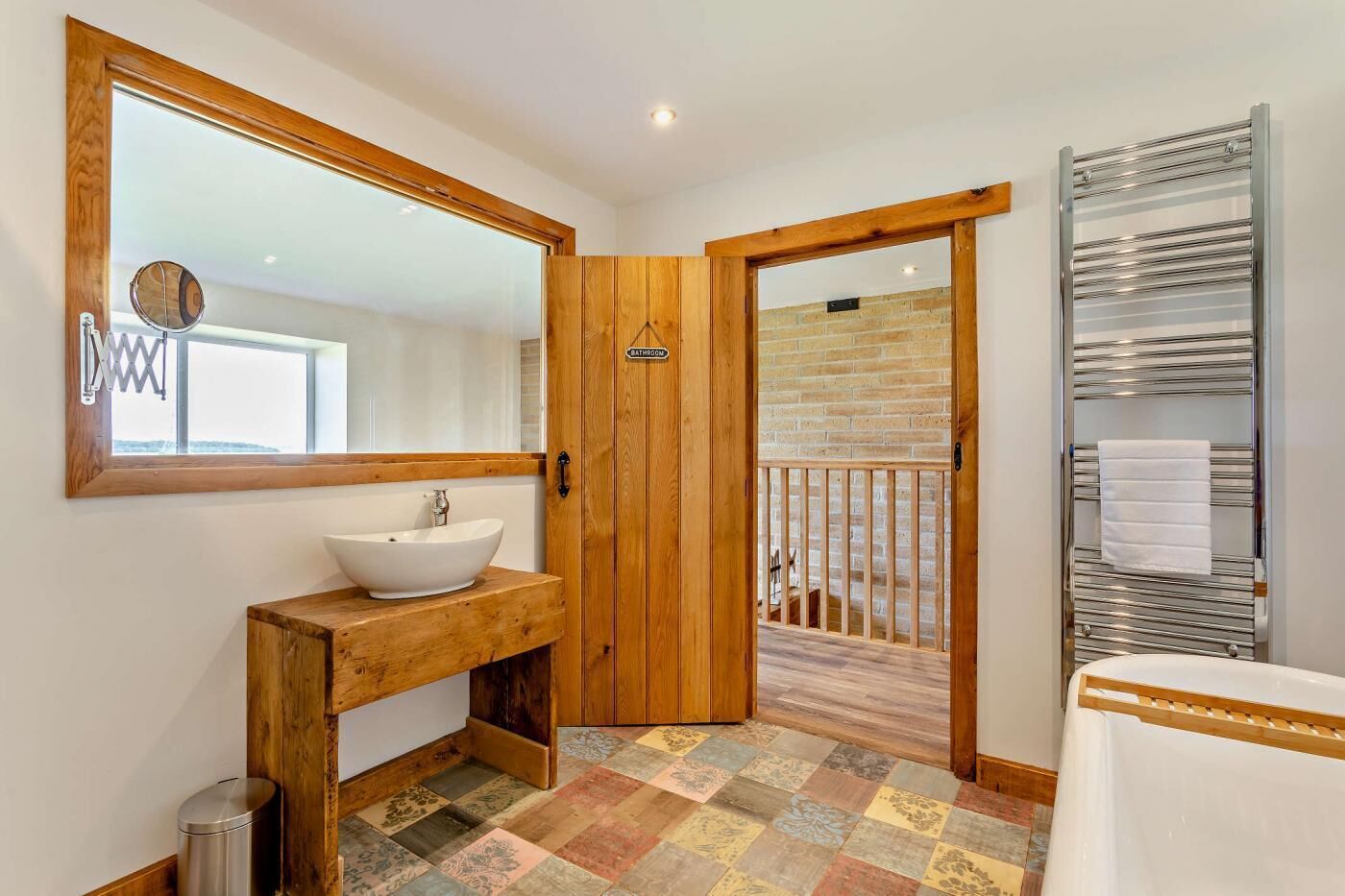 Un baño con tocador de madera, un espejo grande, un lavabo blanco y una zona de ducha con un perchero metálico.