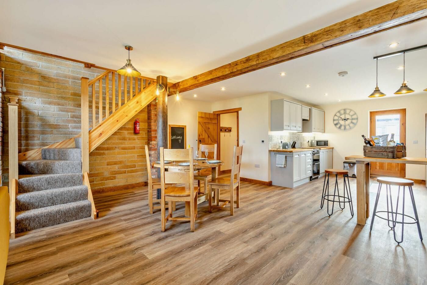 A spacious kitchen with wooden beams, a dining area with a wooden table and chairs, and a staircase with a 'Welcome' sign.