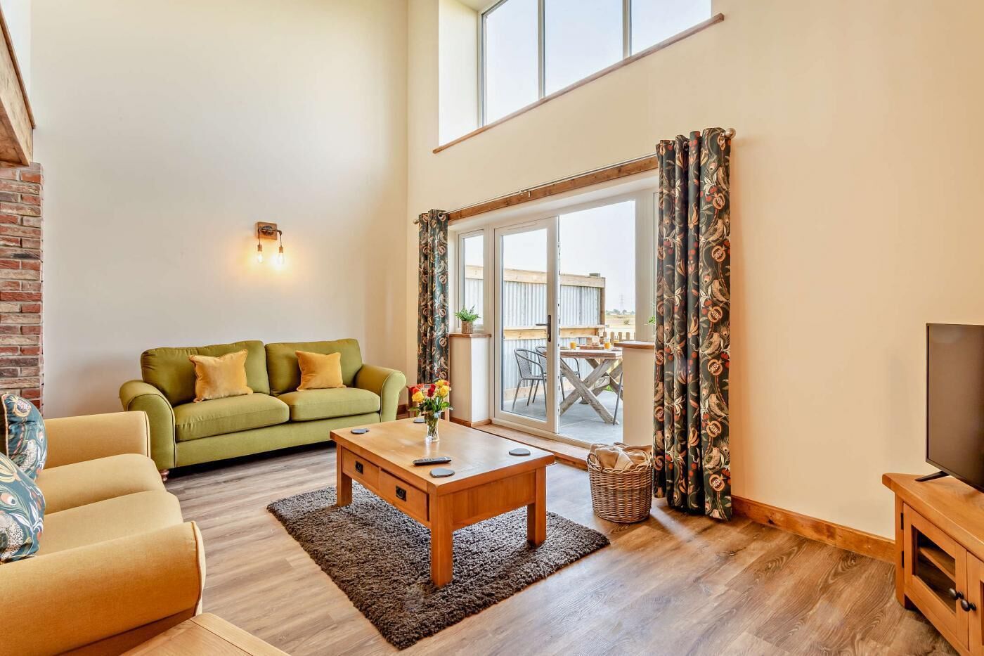 A spacious living room with a green sofa, a wooden coffee table, and a TV stand.