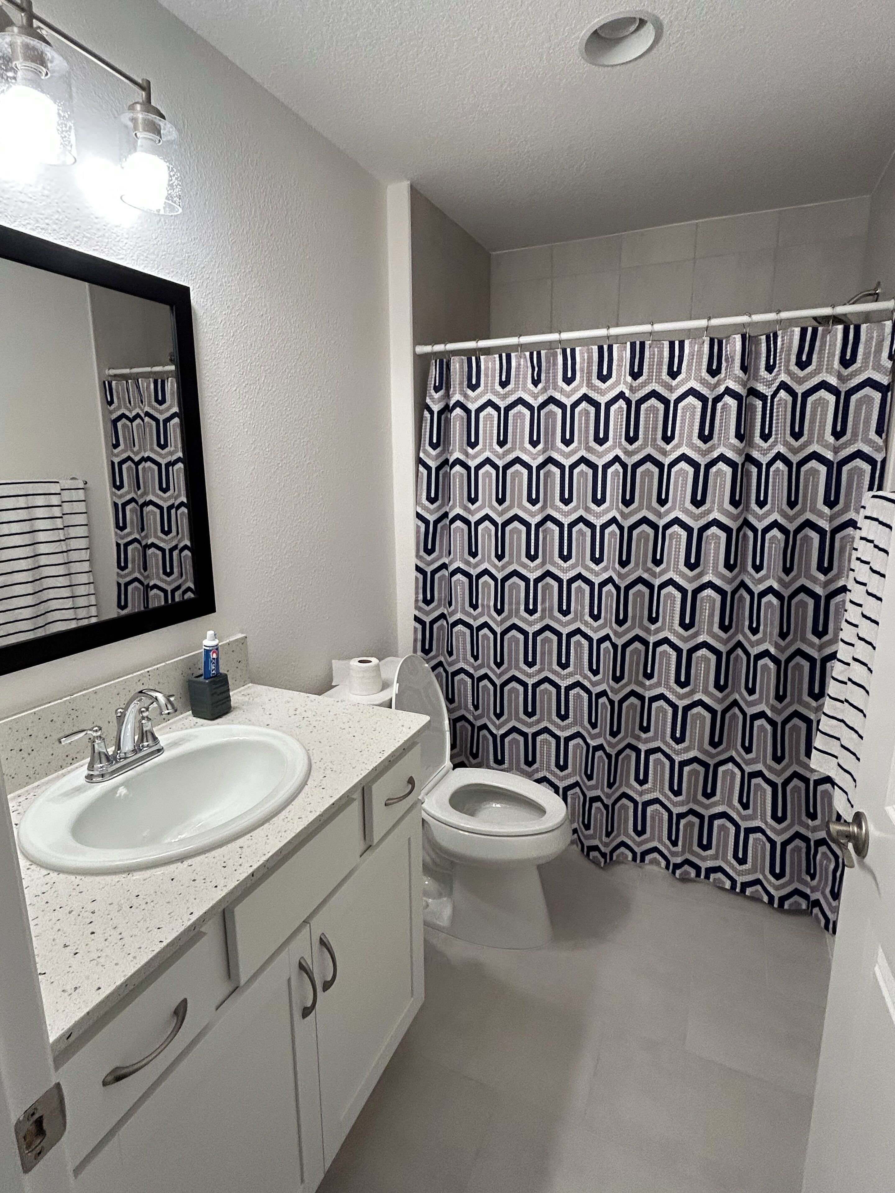 Une salle de bain avec deux lavabos, des toilettes et un rideau de douche orné d’un motif géométrique.