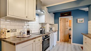 Una cocina con armarios blancos, encimera de madera, microondas y cafetera.