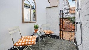En lille udendørs siddeplads med to stole og et bord, en potteplante og en kaffepande.