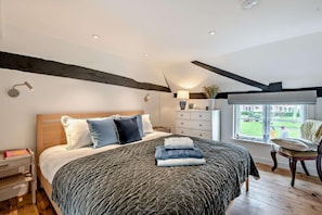 A bedroom with a large bed, bedside tables, a dresser, a chair, and a window with a view. - 1 Bed in Southwold (oc-b27959) (Southwold)