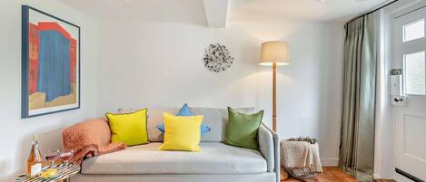 A modern living room with a sofa, colorful cushions, a floor lamp, a painting, and a door with curtains.