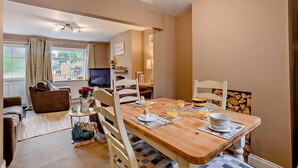 Ein gemütliches Wohnzimmer mit einem Holzesstisch, gedeckt für das Frühstück, einem Fernseher im Hintergrund und einer komfortablen Sitzecke mit Sofa und Sesseln.