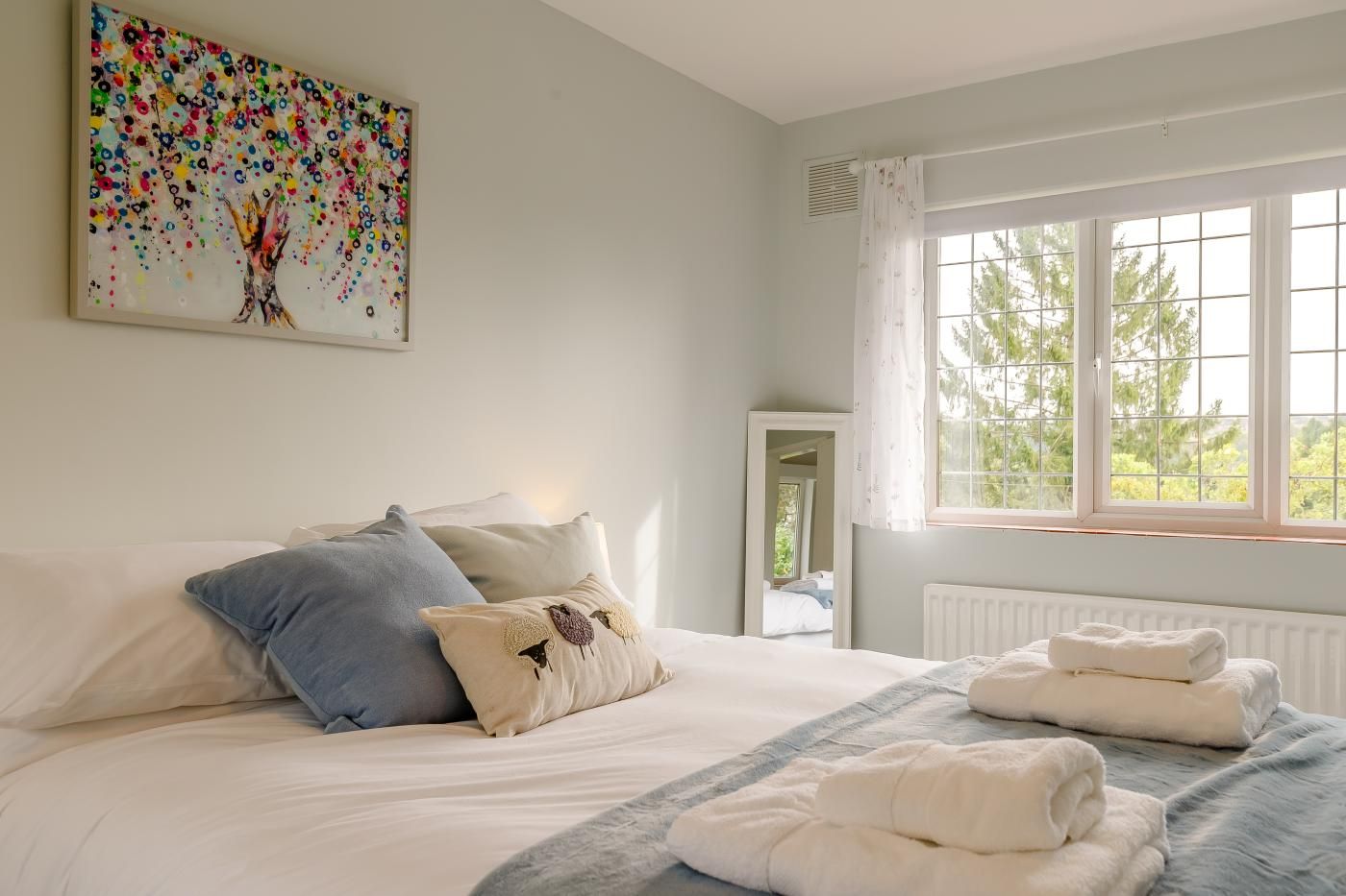 Une chambre à coucher avec un lit, des oreillers, une fenêtre avec des rideaux, un radiateur et un tableau accroché au mur.