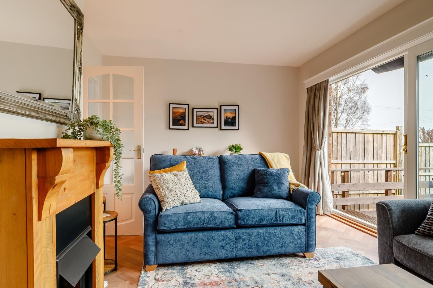 A living room with a blue sofa, a wooden fireplace, and a large window with a view of a wooden deck.