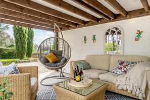 Ein gemütlicher Außenbereich mit einer Hängematte, einer Couch und einem Glastisch mit Flaschen und Gläsern.