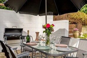 Un patio exterior con una parrilla, mesa de comedor, sillas y un paraguas grande.