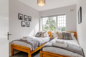 Un dormitorio con dos camas de madera, una ventana con vistas y cuadros enmarcados en la pared.